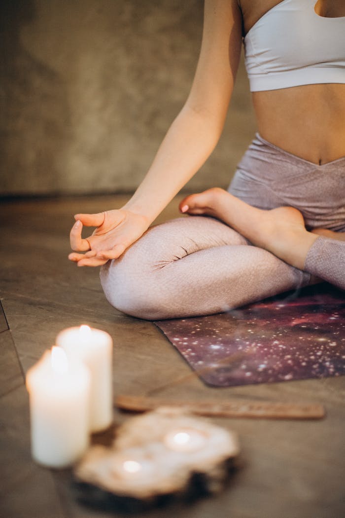 services-01 A woman practicing yoga indoors in lotus pose with candles creating a calming atmosphere.